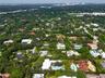 Aerial perspective featuring a flat-roofed estate with a rectangular swimming pool, expansive green lawn, mature trees, and paved driveway