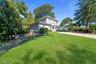 Two-story residence featuring grey horizontal lap siding, a front entry portico with dual columns, a gravel driveway, and mature landscaping