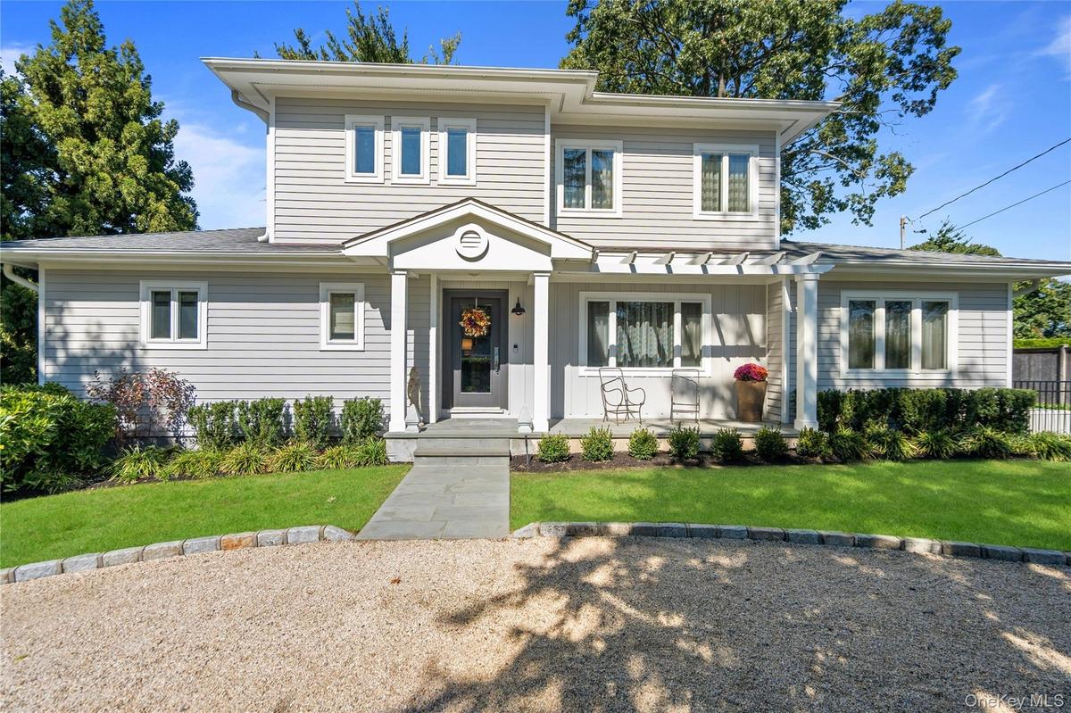 Two-story exterior featuring grey horizontal siding, a covered front porch with a pergola, a stone walkway, and a gravel driveway