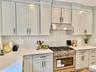 Kitchen featuring stainless steel gas range, under cabinet range hood, tasteful backsplash, and light stone counters