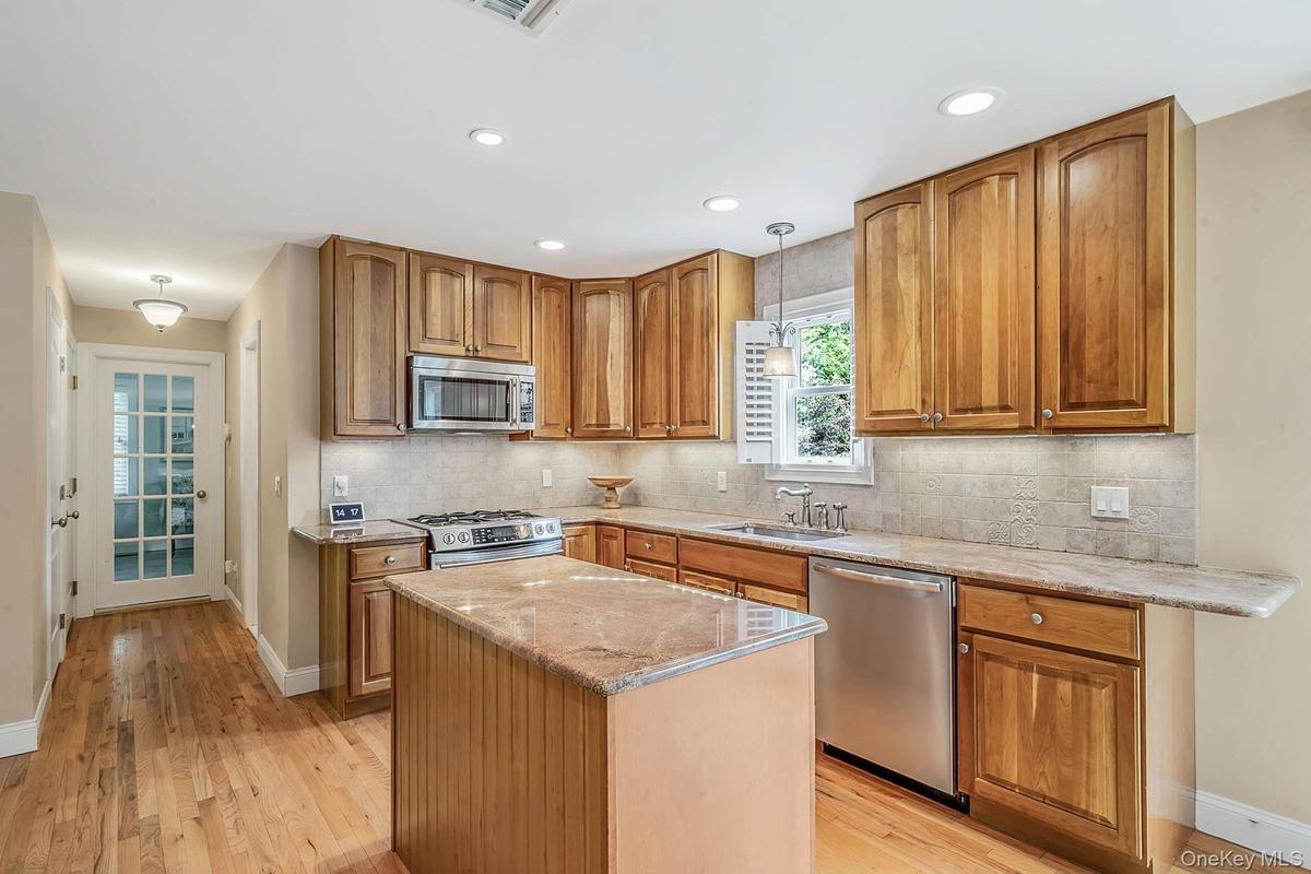 Kitchen featuring wood cabinetry, stone countertops, stone tile backsplash, stainless steel appliances, and wood-finish flooring