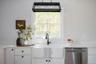 Farmhouse-style apron front sink with a matte black high-arc faucet, white shaker-style cabinetry, solid surface countertops, stainless steel dishwash