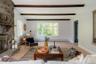 Living area featuring exposed wooden ceiling beams, floor-to-ceiling natural stone fireplace, wood-finish flooring, and multi-pane window