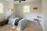 Neutral-toned bedroom featuring light wood-finish flooring, dual windows with natural light, and a matte black ceiling fan