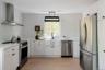 Kitchen featuring white Shaker-style cabinetry, stainless steel appliances, a farmhouse sink with a matte black faucet, wood-finish flooring, and a co