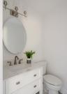 White vanity with stone-composite countertop, undermount sink, brushed nickel widespread faucet, oval mirror, and three-light wall-mounted fixture