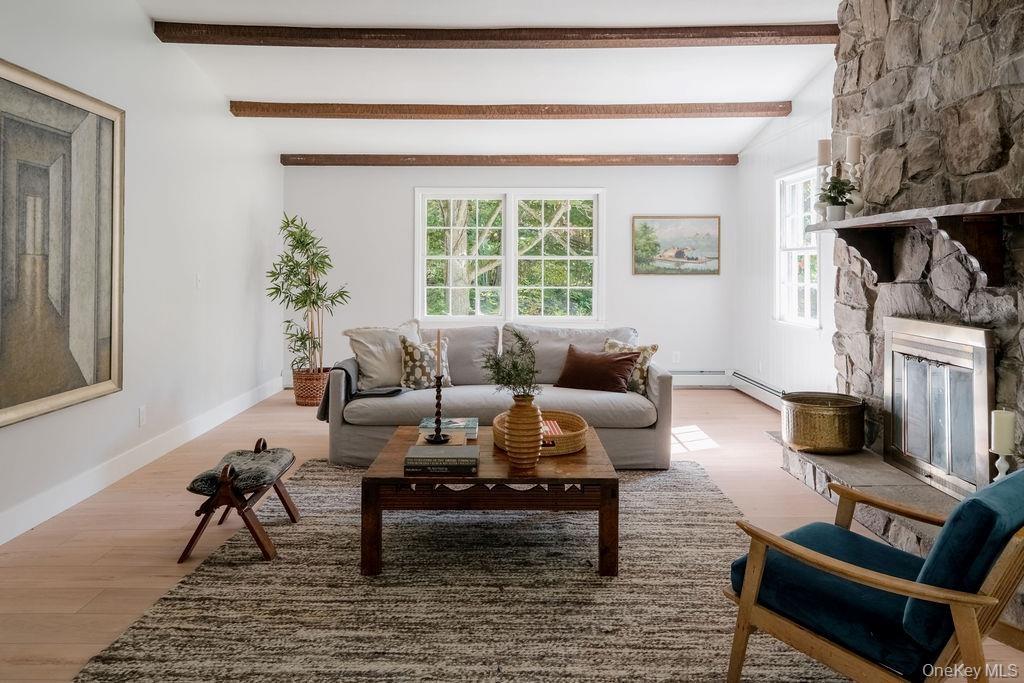Living area featuring wood-finish flooring, exposed ceiling beams, and a floor-to-ceiling stone fireplace with a stone hearth