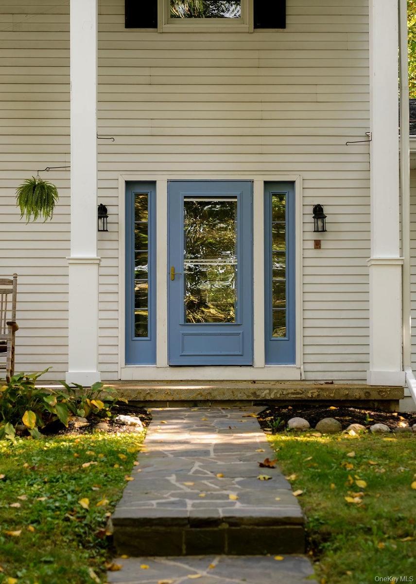 Entryway featuring light-colored horizontal siding, a blue door with glass inlay and matching sidelights, tall white columns, and a flagstone walkway