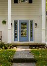 Entryway featuring light-colored horizontal siding, a blue door with glass inlay and matching sidelights, tall white columns, and a flagstone walkway