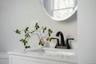White vanity featuring a rectangular integrated sink, white countertop, matte black dual-handle faucet, and circular wall-mounted mirror