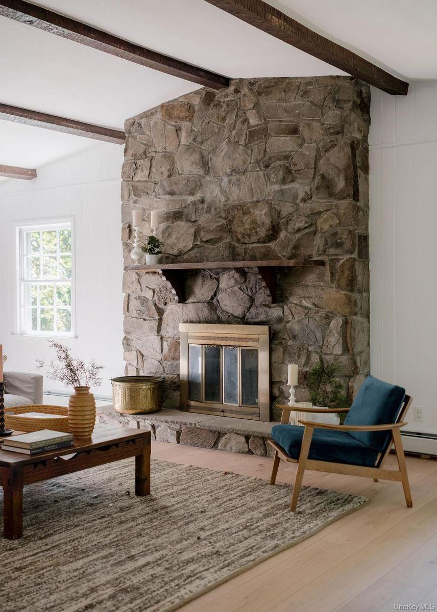 Floor-to-ceiling stone fireplace featuring a stone hearth, a wood-finish mantel, dark exposed ceiling beams, and wood-finish flooring