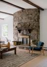 Floor-to-ceiling stone fireplace featuring a stone hearth, a wood-finish mantel, dark exposed ceiling beams, and wood-finish flooring