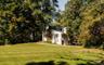 Multi-level exterior with light-colored siding, brick chimney, shuttered windows, and a generous lawn surrounded by mature trees