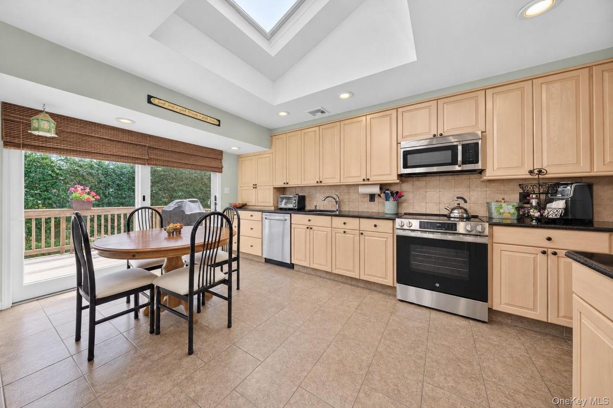 Kitchen featuring light wood cabinetry, stone countertops, stainless steel appliances, a skylight, and tile flooring