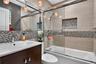 Bathroom featuring a vanity with an integrated rectangular sink, glass-enclosed shower and tub combination, multi-colored mosaic tile accents, wall-mo