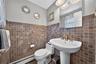 Pedestal sink with a brass-finish widespread faucet, square tile wainscoting, large frameless wall mirror, and dual-bulb vanity light fixture