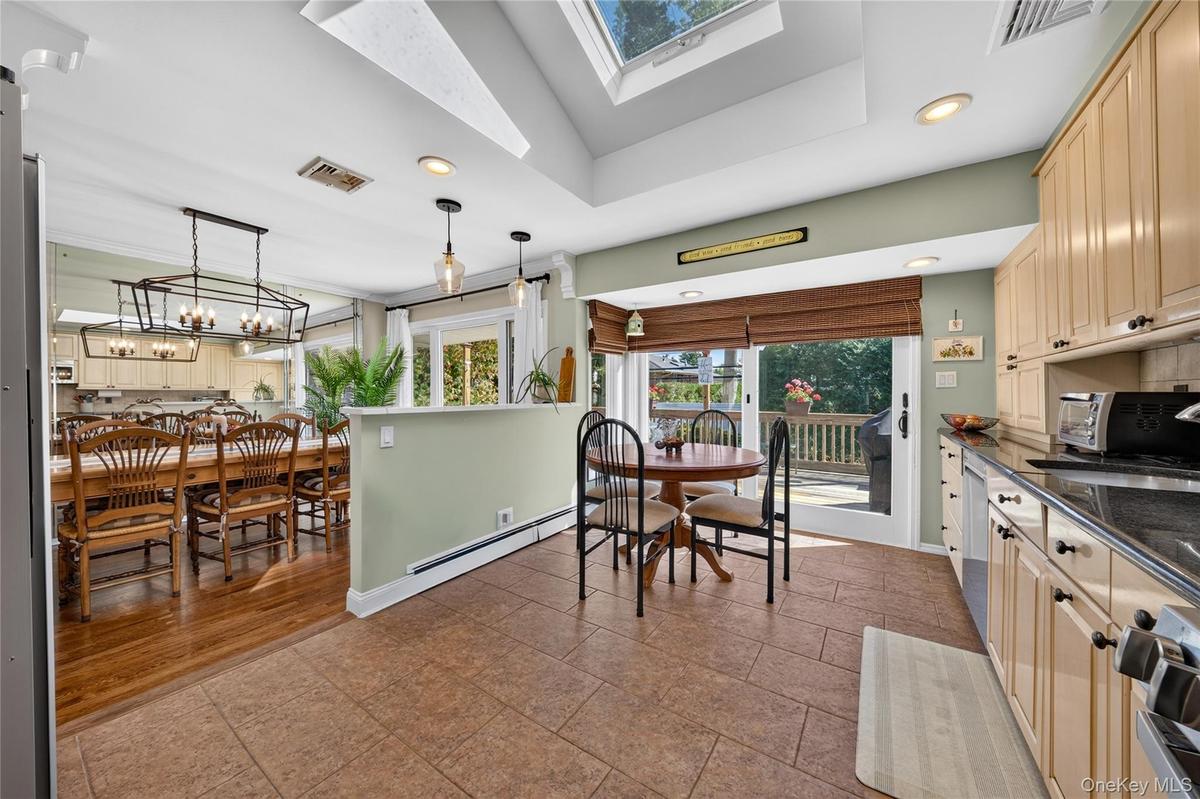 Kitchen featuring ceramic tile flooring, built-in light-finish cabinetry, dark solid-surface countertops, recessed lighting, and a skylight