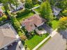 Aerial perspective of a residence featuring a brown shingle roof with a chimney and skylights, an elevated rear deck, a paved driveway, and mature lan