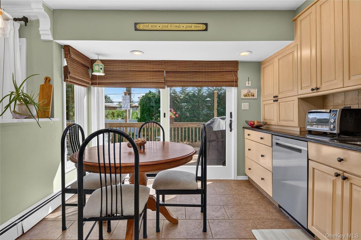 Kitchen featuring light wood cabinetry, dark stone countertops, stainless steel dishwasher, tile flooring, and sliding glass doors with integrated win