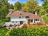 Backyard featuring a wood deck with railing, a paved circular patio, shingle siding, a skylight, and a brick chimney