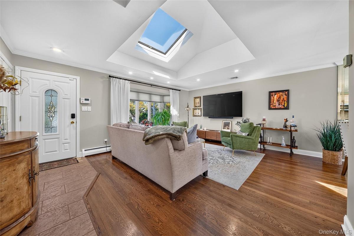Vaulted ceiling featuring a large rectangular skylight, wood-finish flooring, recessed lighting, and a front entry door with decorative glass paneling