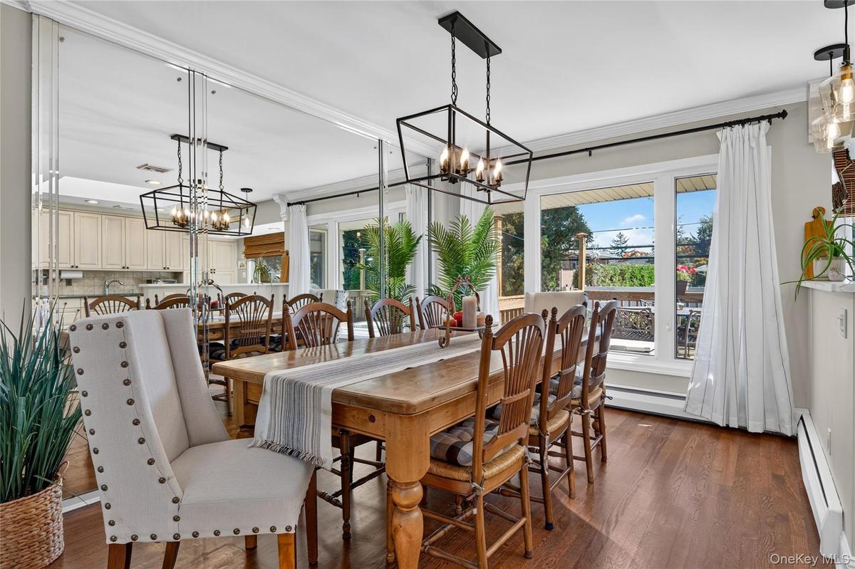 Dining area featuring wood-finish flooring, floor-to-ceiling mirrored wall paneling, crown molding, and a geometric metal pendant chandelier