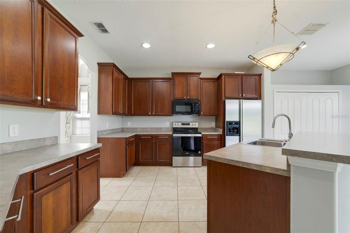 Step through an arched doorway into the spacious Kitchen with ABUNDANT STAGGERED CABINETRY and generous counter space.