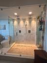 Walk-in shower featuring a frameless glass enclosure, dual rain-style showerheads, hand-held sprayer, large-format stone-look wall tile, and a texture