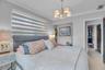 Neutral-toned bedroom featuring crown molding, a five-arm metal chandelier, and layered dual-fabric window shades