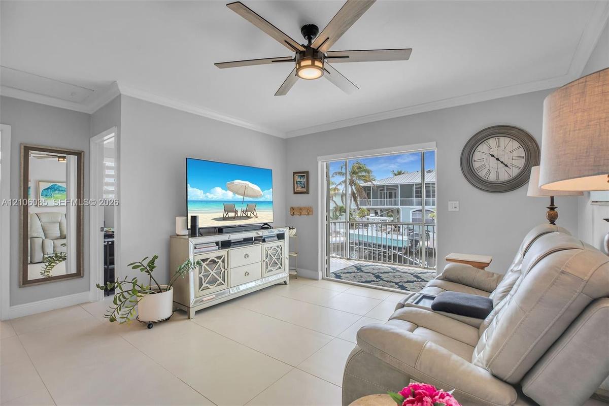 Living area featuring large-format tile flooring, a multi-blade ceiling fan with integrated lighting, crown molding, and sliding glass doors opening t