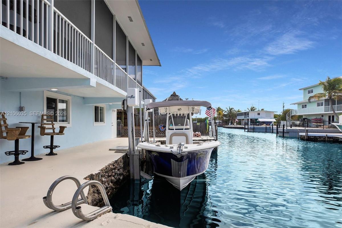 Waterfront property featuring a concrete seawall, private boat lift, and a covered lower-level concrete patio