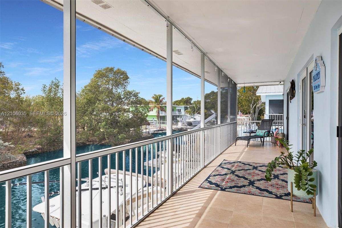 Covered screened-in balcony featuring tile flooring and metal railings, overlooking a canal with private dock access