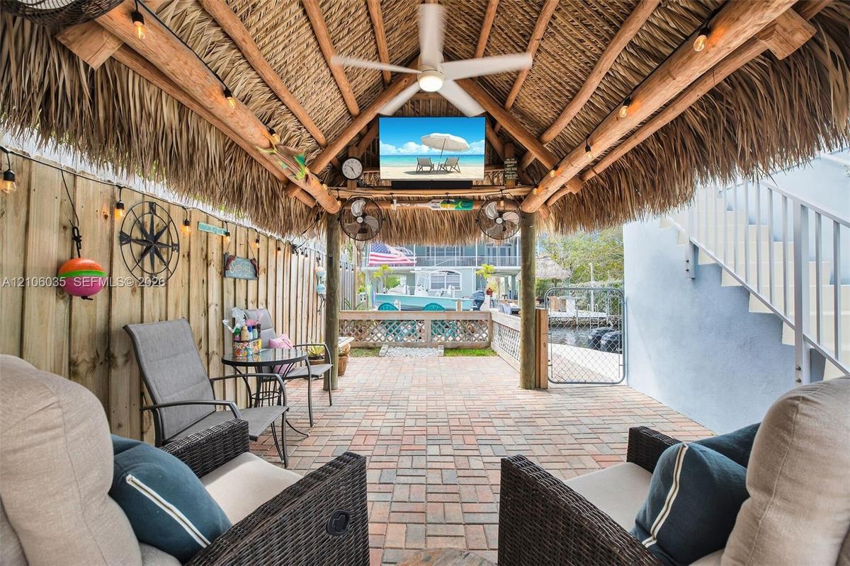 Covered patio featuring a thatched roof, brick paver flooring, ceiling fan, and string lighting