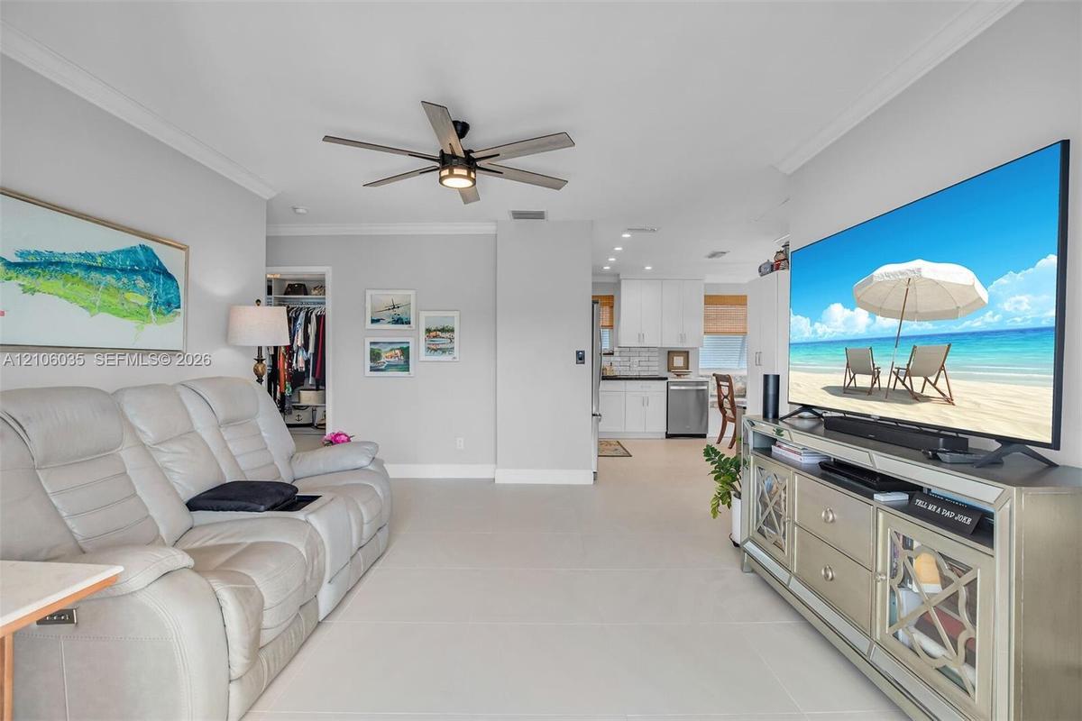 Open living area featuring large-format tile flooring, crown molding, and a modern multi-blade ceiling fan with integrated lighting