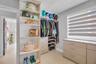 Custom closet organization system featuring light-toned cabinetry, integrated shelving units, tiered storage drawers, and a window fitted with adjusta