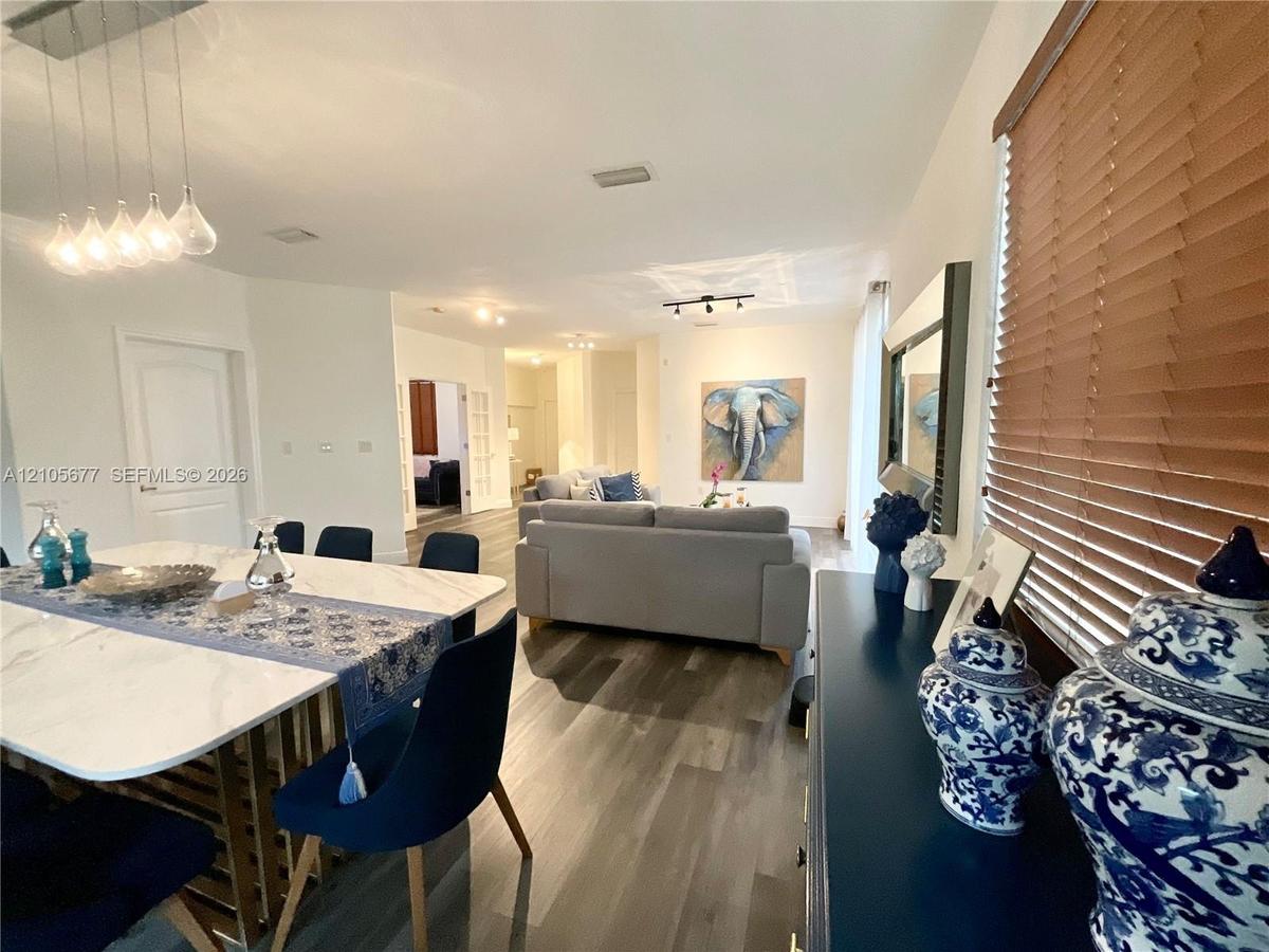 Open-concept interior featuring wood-finish flooring, multi-pendant lighting, and horizontal window blinds