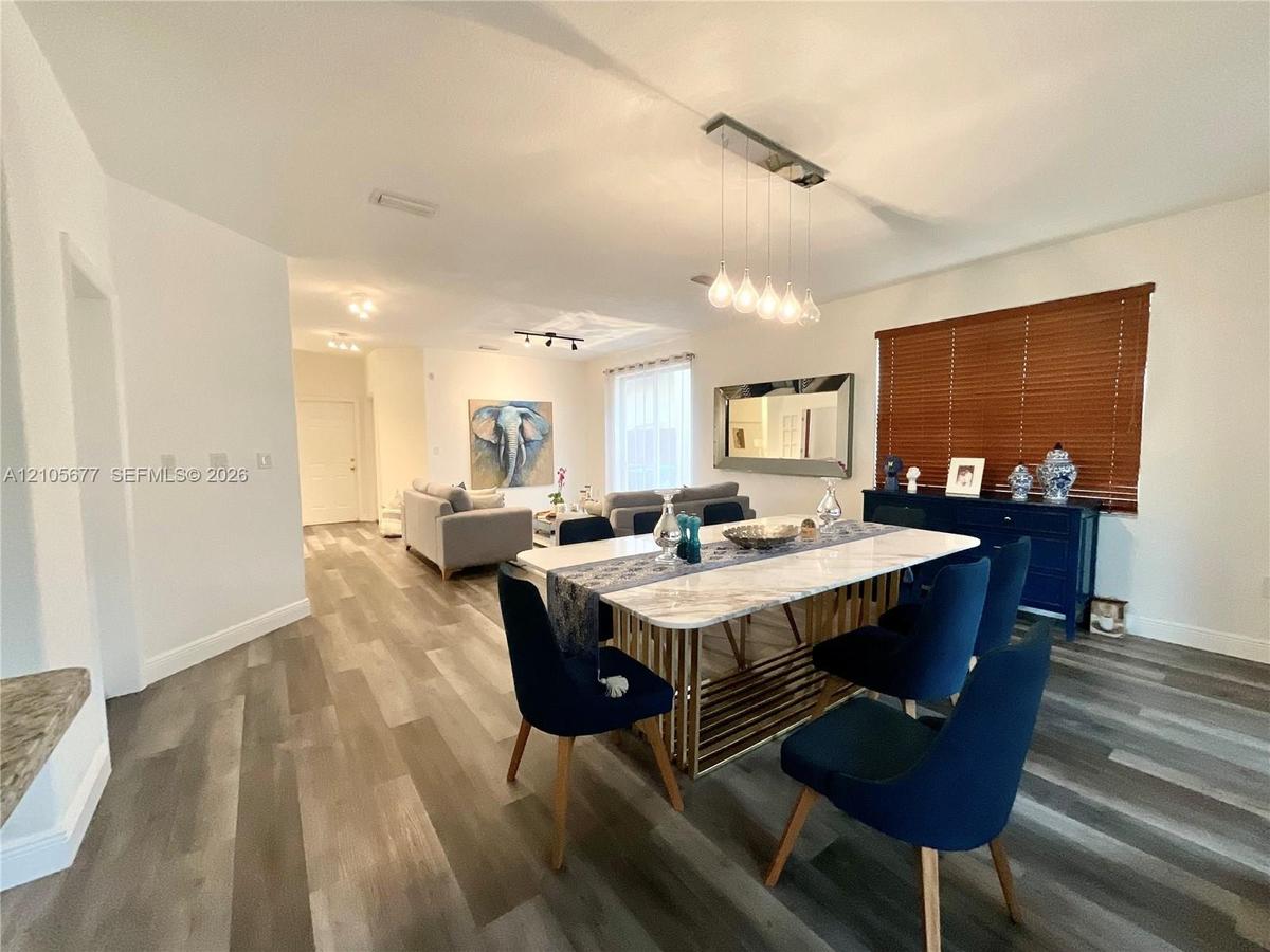 Open-concept living and dining area featuring multi-tonal wood-finish flooring, recessed lighting, a modern multi-pendant light fixture, and horizonta