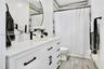 White vanity with solid-surface countertop and matte black hardware, integrated sink, circular mirror, and wood-finish tile flooring