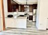 Kitchen featuring dark wood cabinetry, stone-surface countertops, subway tile backsplash, stainless steel appliances, and wood-finish flooring