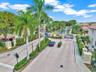 Gated community entrance featuring paver-stone driveways, ornamental stone pillars, professional landscaping with mature palm trees, and structural se