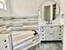 Bathroom featuring a white dual-sink vanity with louvered cabinets, a circular mirror, corner soaking tub, horizontal-patterned wall tiling, and wood-