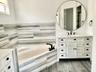 White vanity with louvered cabinet doors, quartz countertop, corner soaking tub with matte black faucet, and horizontal wall tile surround
