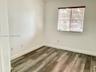 Neutral-toned interior room featuring wood-finish flooring, white walls, and a window with horizontal blinds