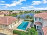 Stucco exterior with tile roofing, rectangular swimming pool, stone-paved pool deck, and landscaped grounds surrounding a water feature with fountain