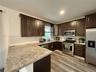 Kitchen featuring dark wood cabinetry, stone-finish countertops, stainless steel appliances, white subway tile backsplash, and wood-finish flooring