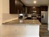 Kitchen featuring dark wood-finish cabinetry, stone-style countertops, white subway tile backsplash, stainless steel appliances, and wood-finish floor