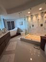 Bathroom featuring a walk-in glass-enclosed shower with large-format stone-patterned wall tile, pebble-texture shower flooring, a freestanding soaking