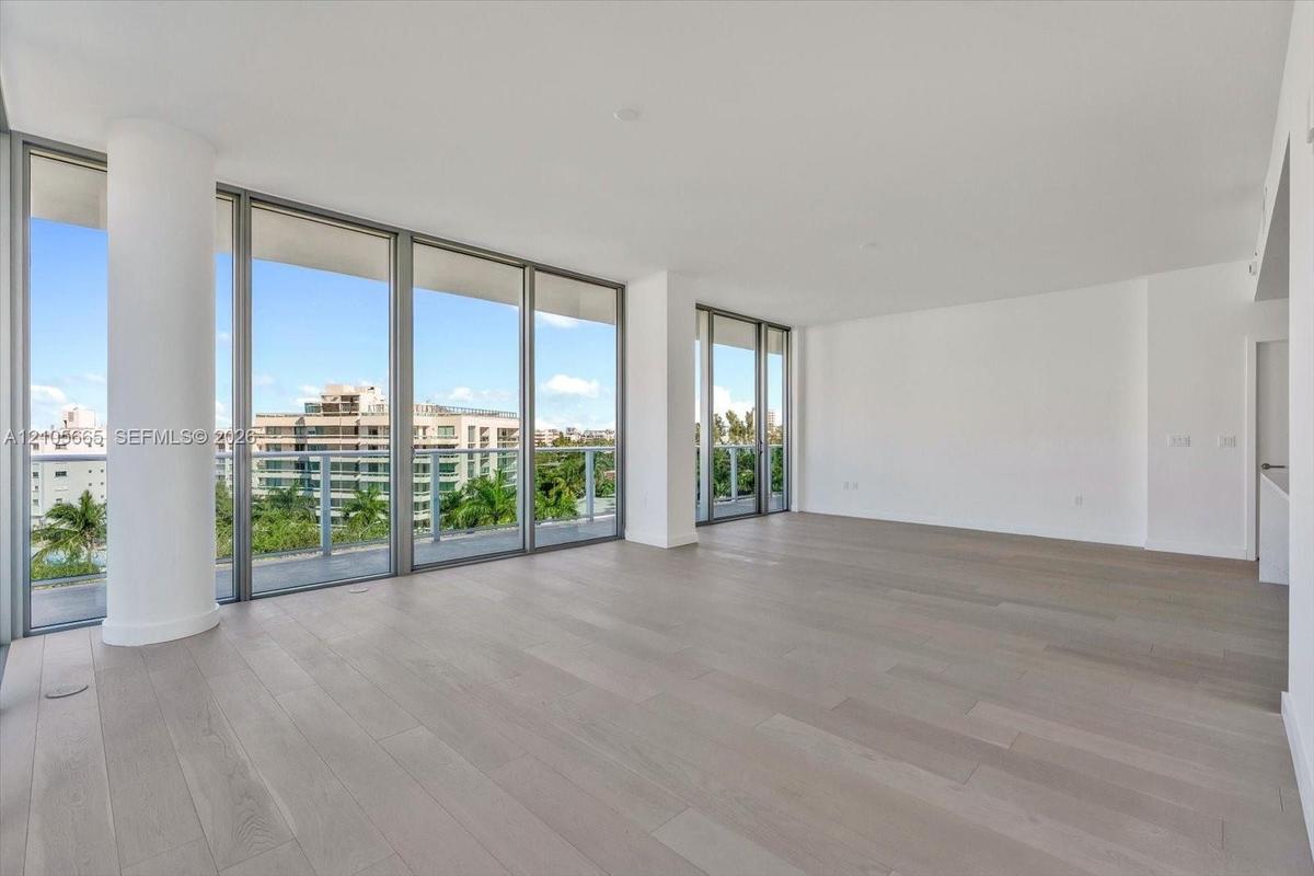 Expansive living area featuring floor-to-ceiling glass walls, wood-finish flooring, structural columns, and an exterior balcony