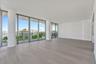 Expansive living area featuring floor-to-ceiling glass walls, wood-finish flooring, structural columns, and an exterior balcony