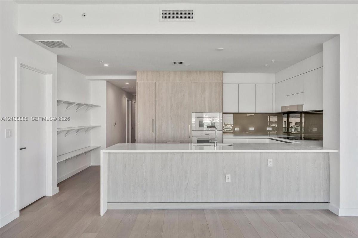 Kitchen featuring a waterfall-edge quartz countertop, two-tone cabinetry with wood-finish and flat-panel white finishes, integrated appliances, and a 